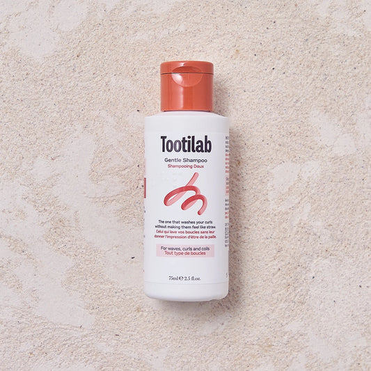 Tootilab shampoo bottle with red cap on a beige background