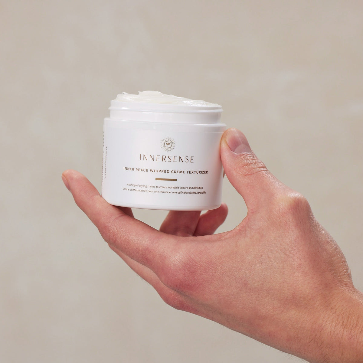 Hand holding a white jar of Innersense product against a neutral background