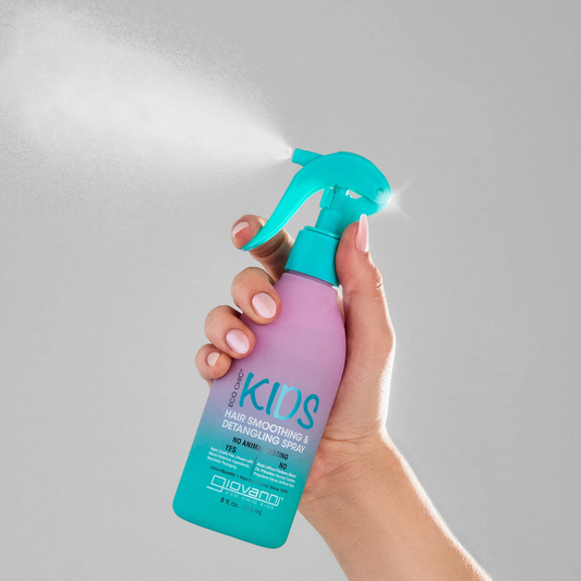 Hand holding a purple and teal spray bottle labeled 'KIDS' against a light gray background