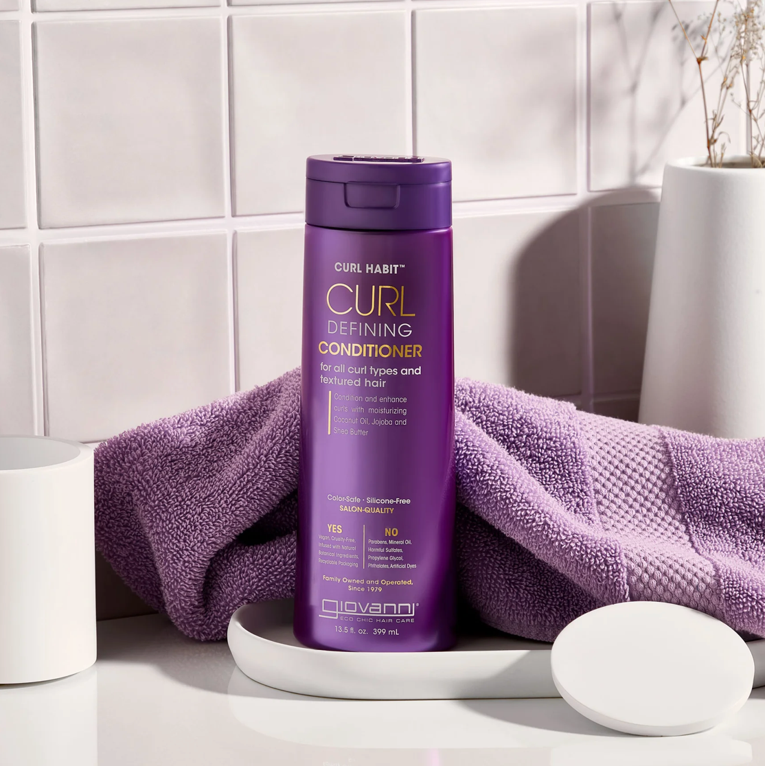 Purple bottle of Curl Habit conditioner on a white surface with a purple towel.