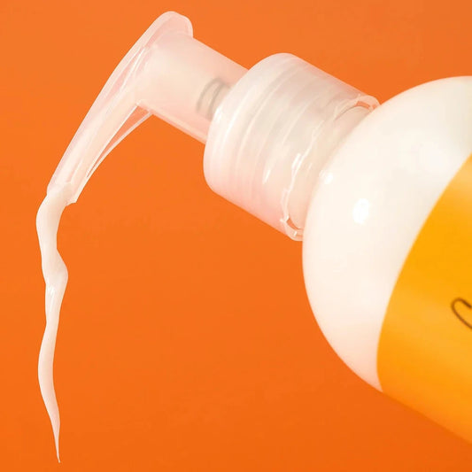 Bottle of curl cream with pump being used on an orange background