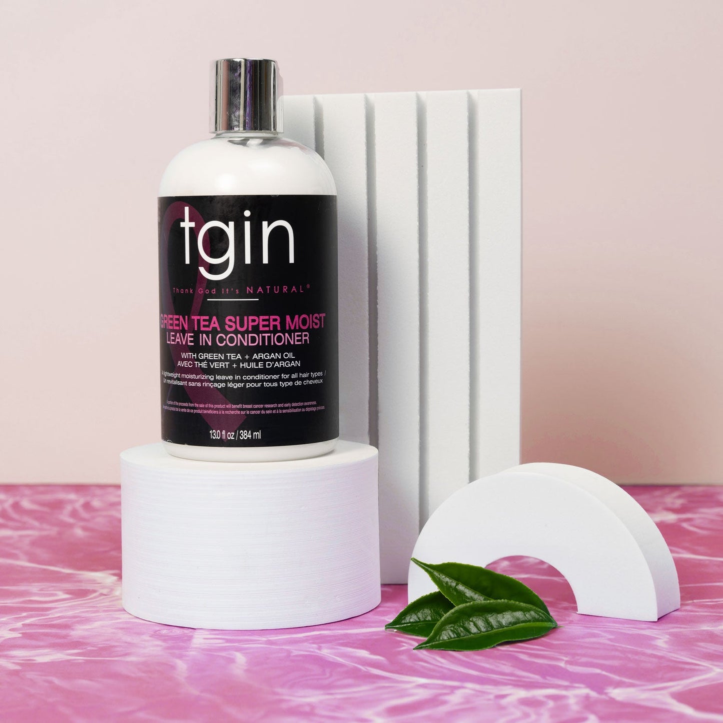 tgin Green Tea Super Moist Leave-In Conditioner bottle on a pink background with green leaves.