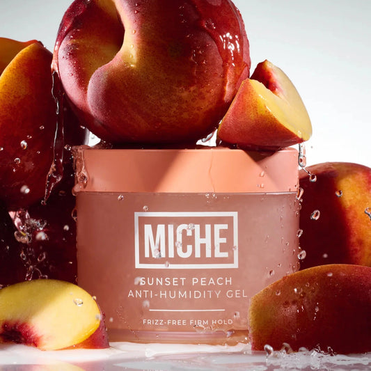 A jar of MICHE Sunset Peach Anti-Humidity Gel surrounded by fresh peach slices and water droplets on a light gray background.
