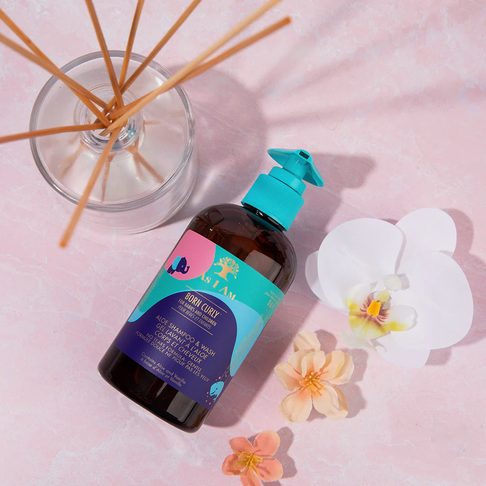 Bottle of As I Am hair care product with flowers and reeds on a pink background