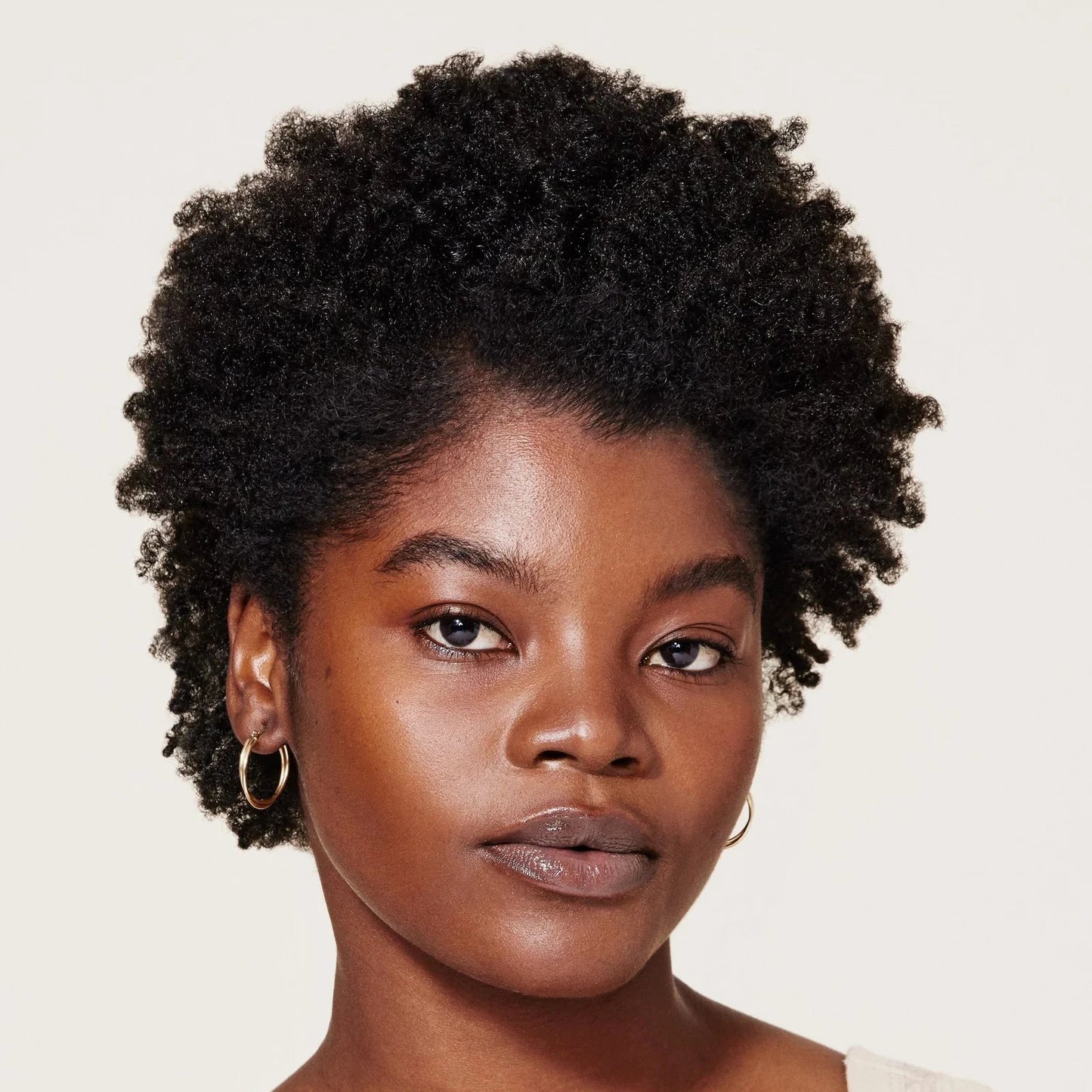 Woman with short, curly hair wearing a beige top against a plain background