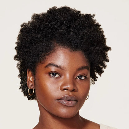 Woman with short, curly hair wearing a beige top against a plain background