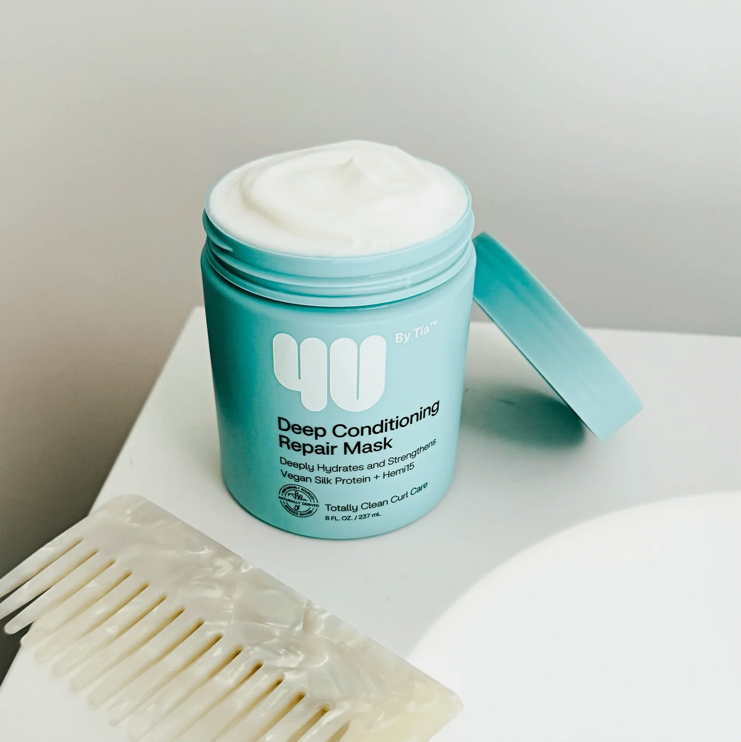 Blue jar of deep conditioning repair mask with a white comb on a light surface.