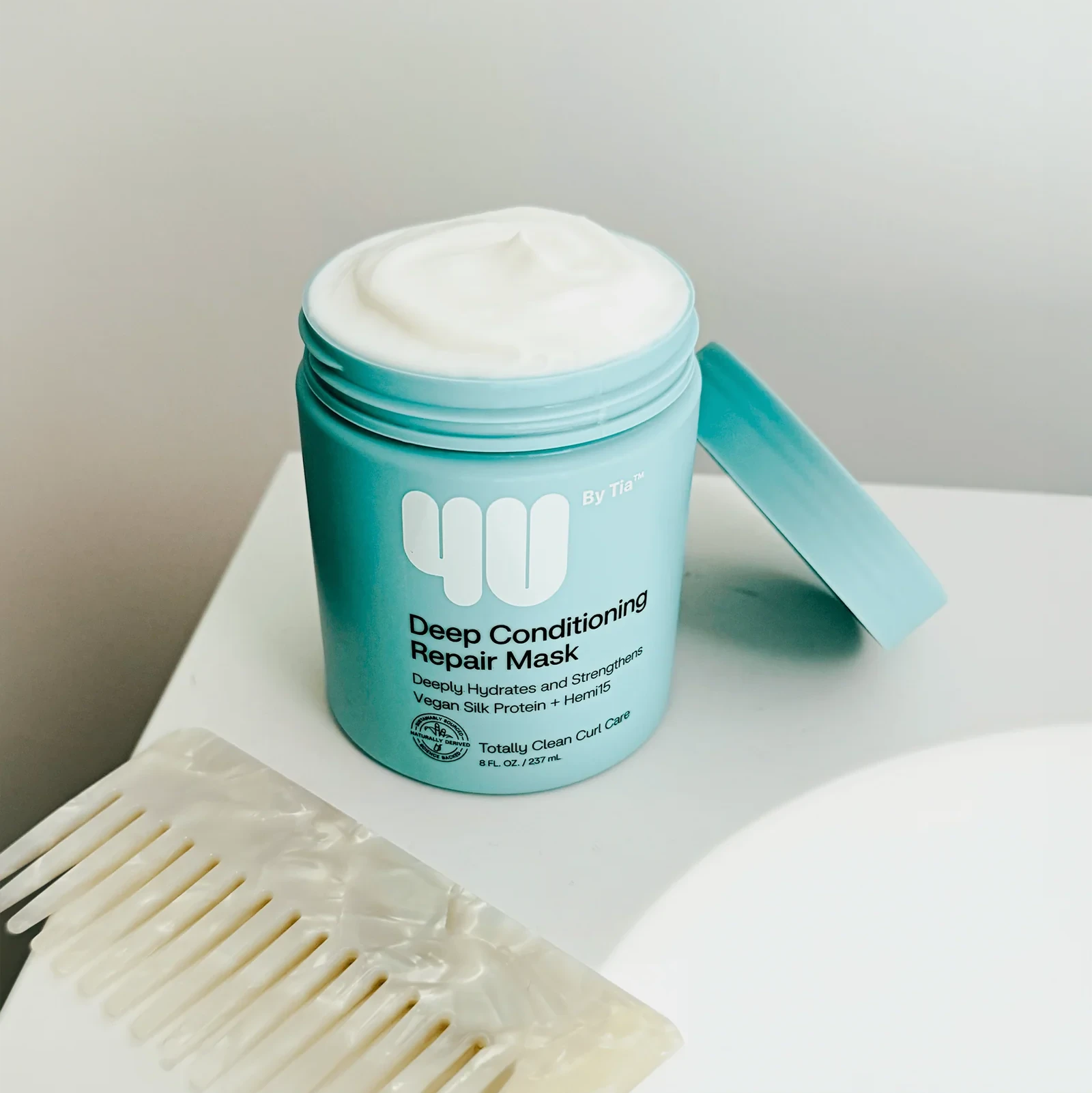 Blue jar of deep conditioning repair mask with a white comb on a light surface.