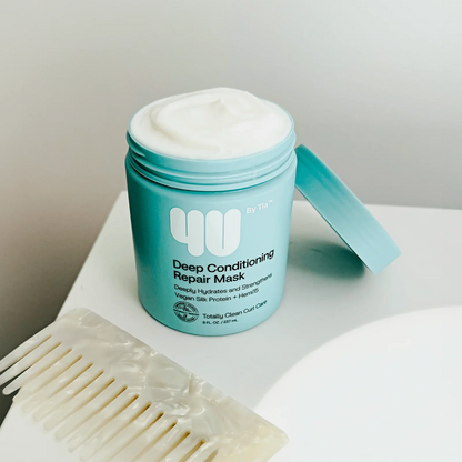 Blue jar of deep conditioning repair mask with a white comb on a light surface.