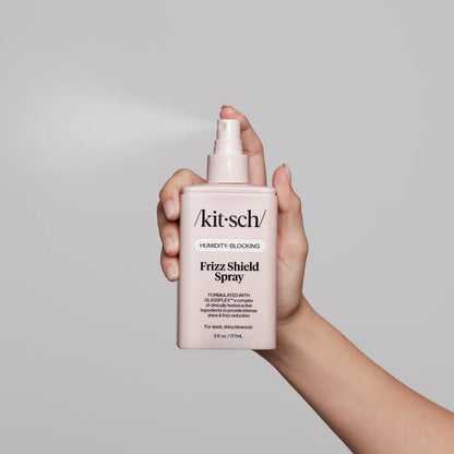Hand holding a pink bottle of 'kitsch' Frizz Shield Spray against a gray background