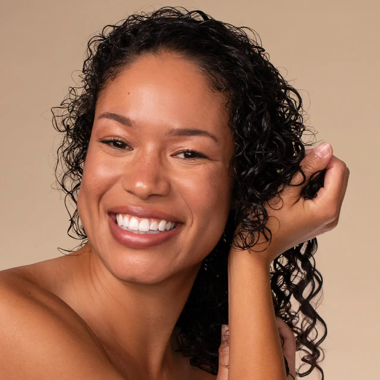 Woman with curly hair smiling against a beige background