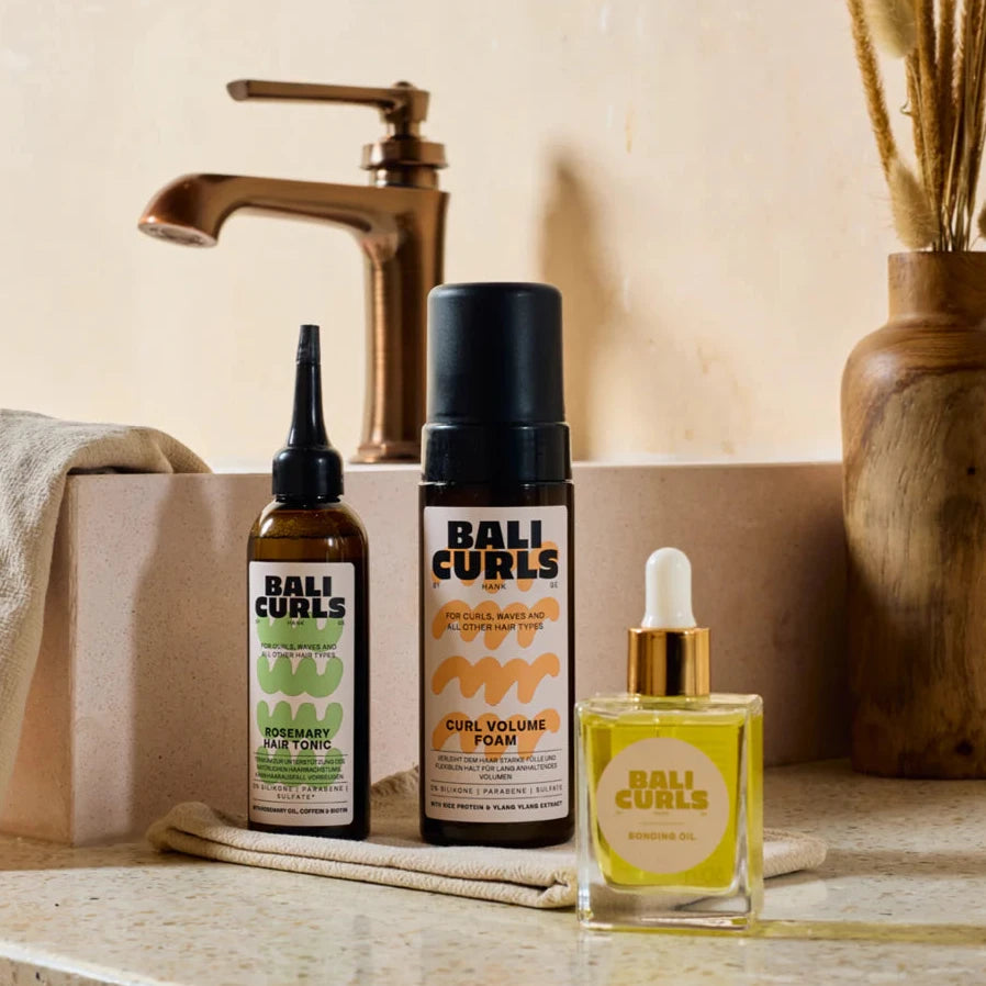 Bali Curls hair care products on a bathroom counter with a faucet and towel in the background.