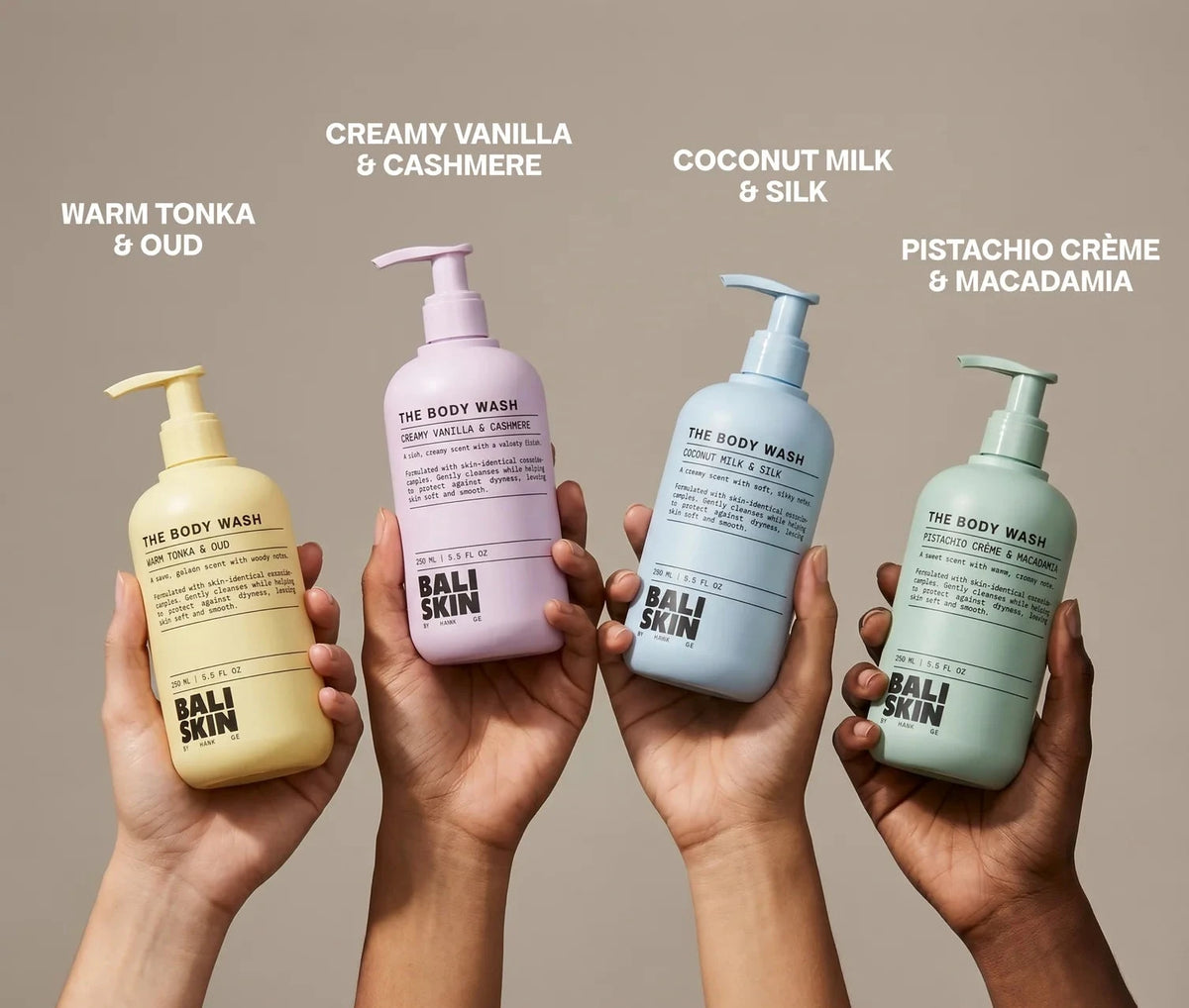 Four pump bottles of Bali Skin body wash are held up by four hands against a warm beige background. Each hand holds a different colored bottle: yellow, lavender, light blue, and sage green.