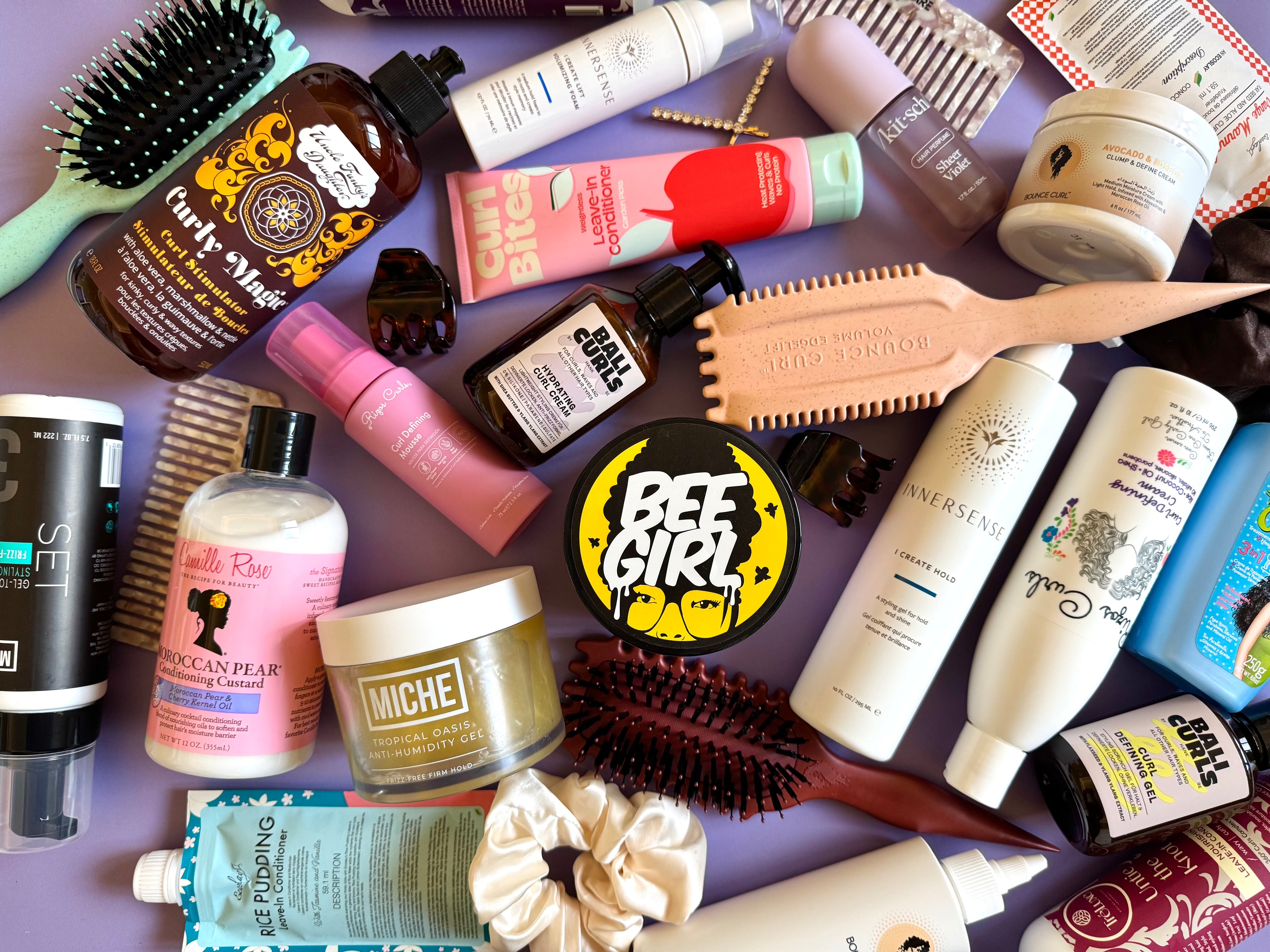 Assorted hair care products including bottles, jars, and brushes on a purple surface.