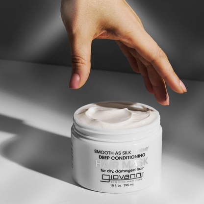 Hand reaching towards a jar of Giovanni hair mask on a neutral background