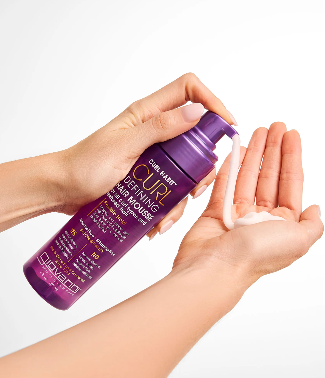 Purple bottle of hair product being held with a hand on a white background