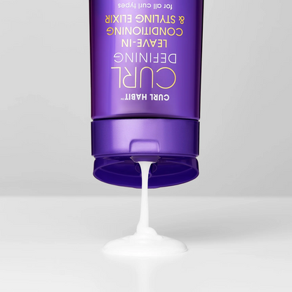Purple bottle of hair product with white cream being squeezed out on a light gray background