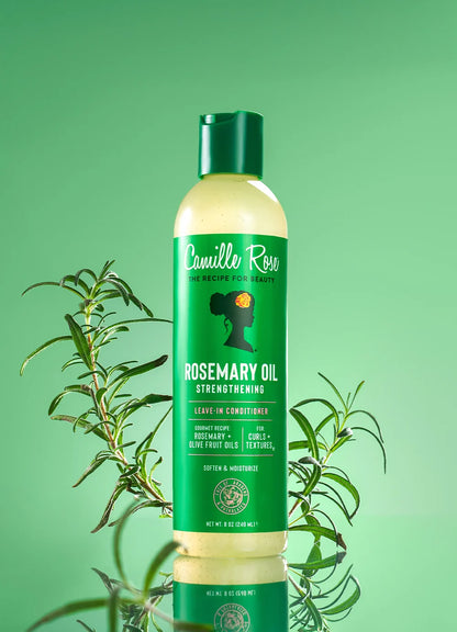 A bottle of Camille Rose Rosemary Oil Strengthening Leave-In Conditioner, featuring a green cap and a green label with white text, set against a solid green background with rosemary sprigs.