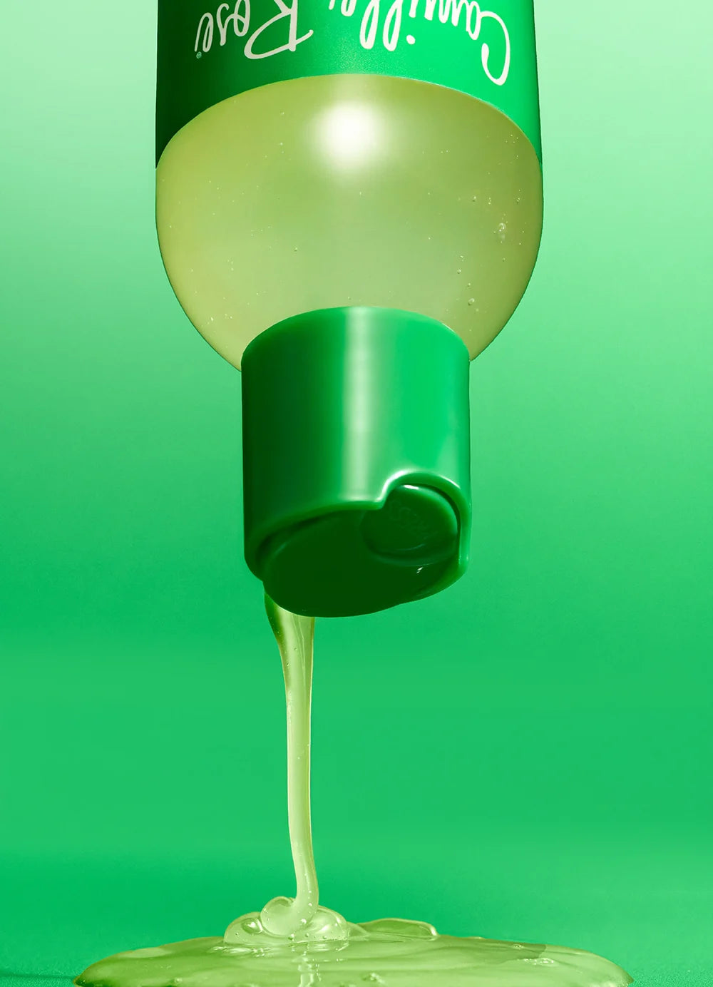 A close-up of a green squeeze bottle dispensing a thick, translucent pale green gel or honey-like substance, with the bottle and dripping product shown against a solid green background.