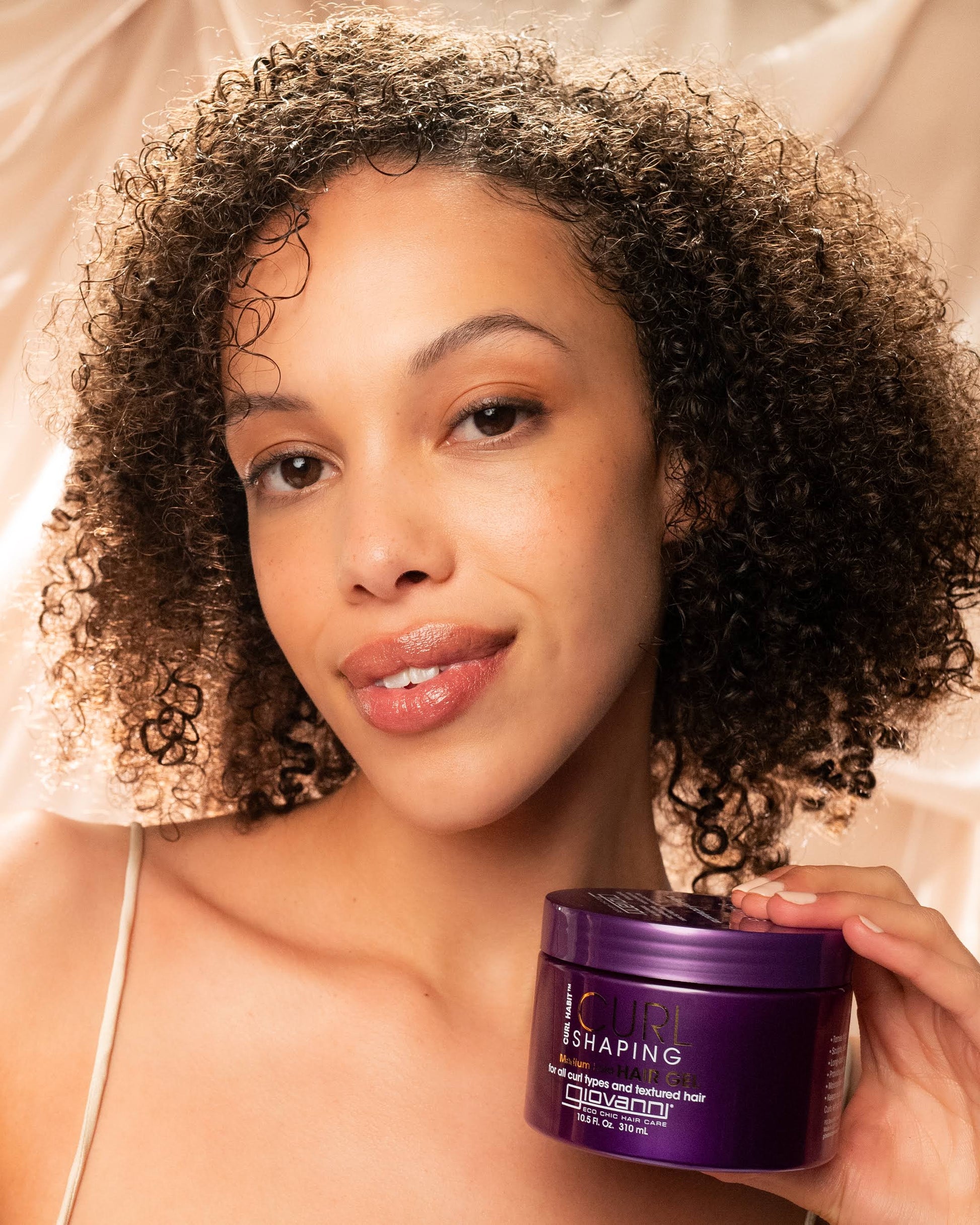 Woman holding a purple hair product container with a neutral background